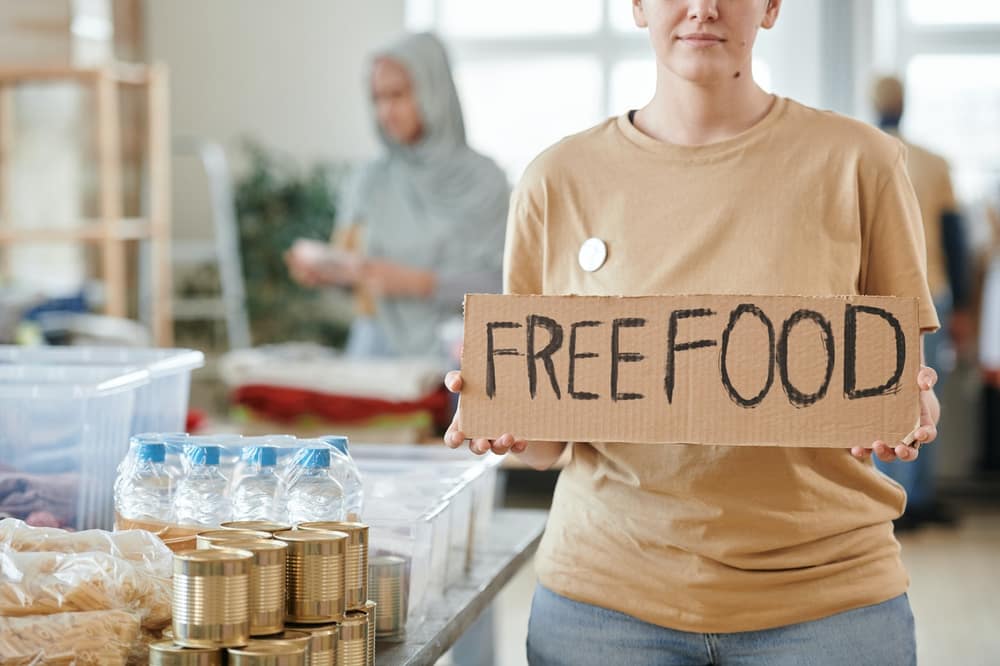 Volunteer holding a free food sign beside donated supplies
